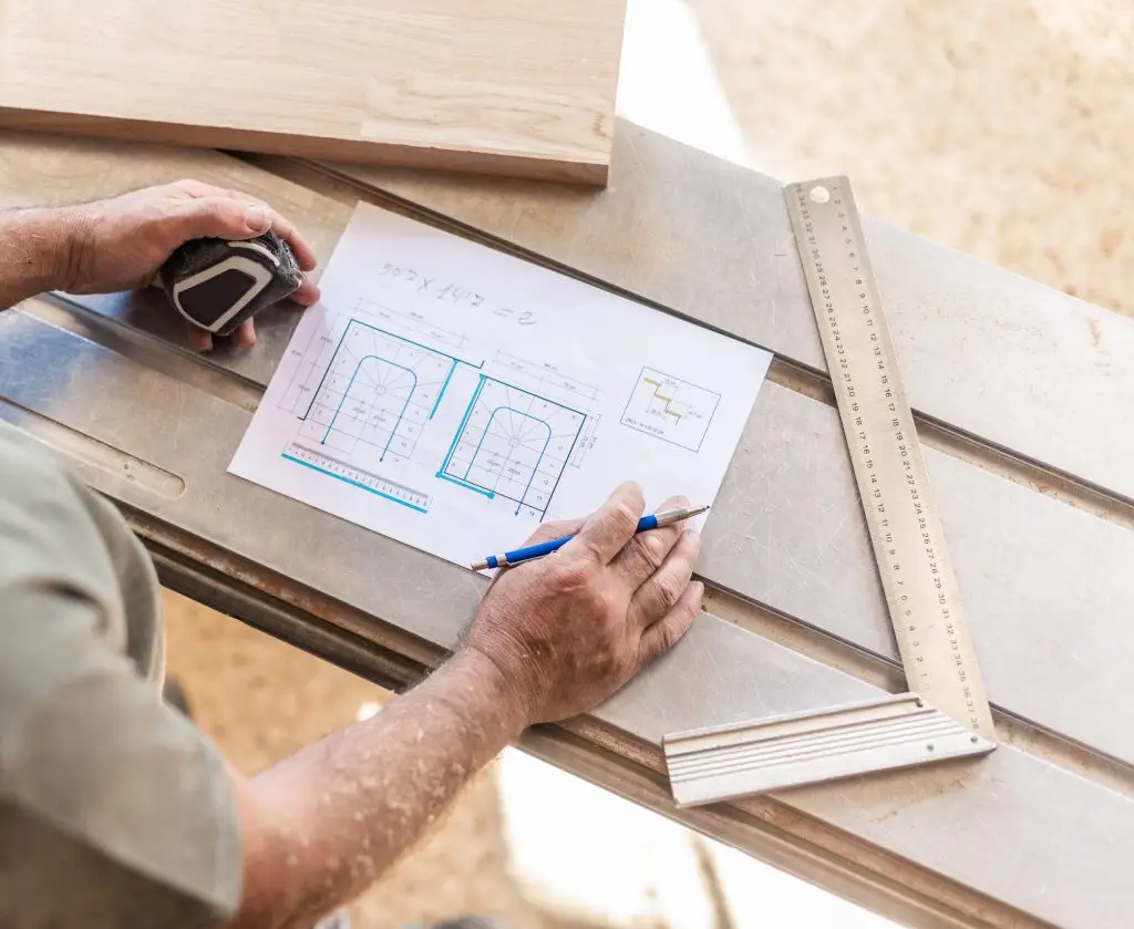 Artisan annotant un plan de projet pos&eacute; sur des planches de bois