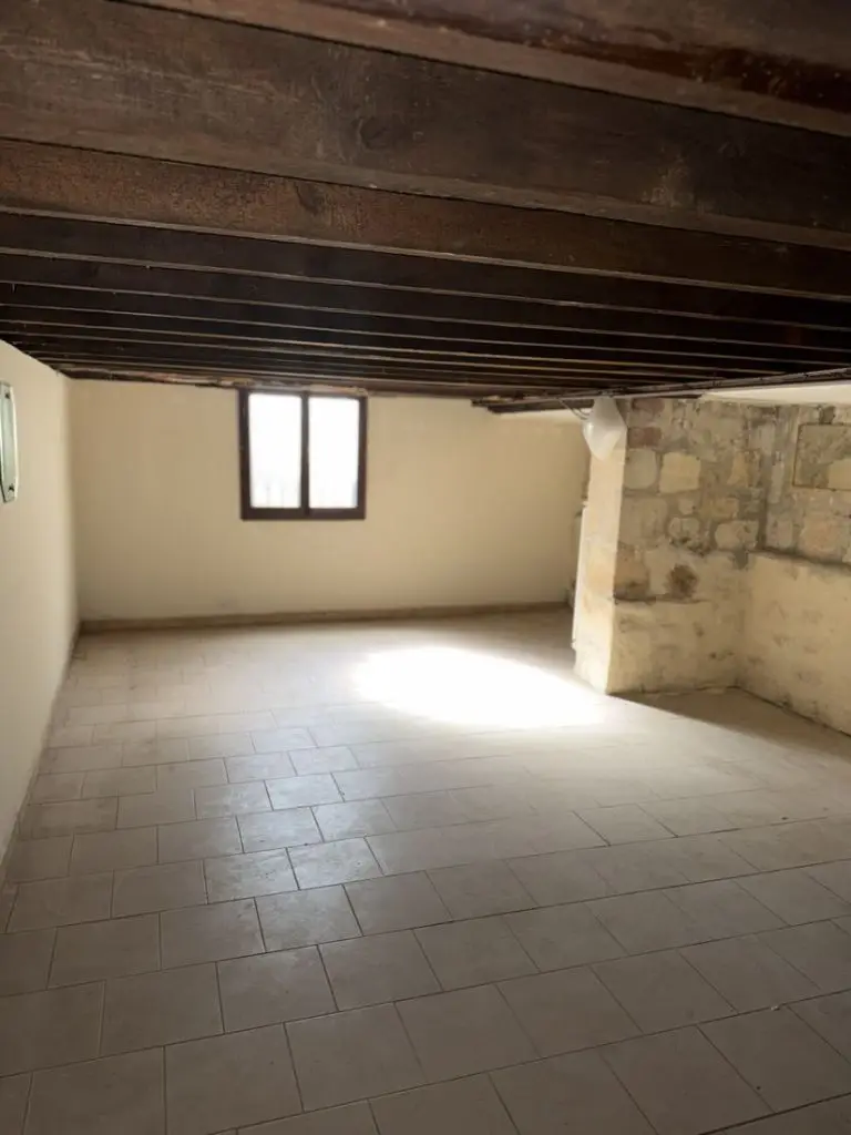 Cave d’une maison ancienne avec murs en pierre, plancher en bois et fenêtre sur rue